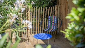 Un patio exterior con cerramiento de madera, una mesa de metal azul y una silla tejida de colores.