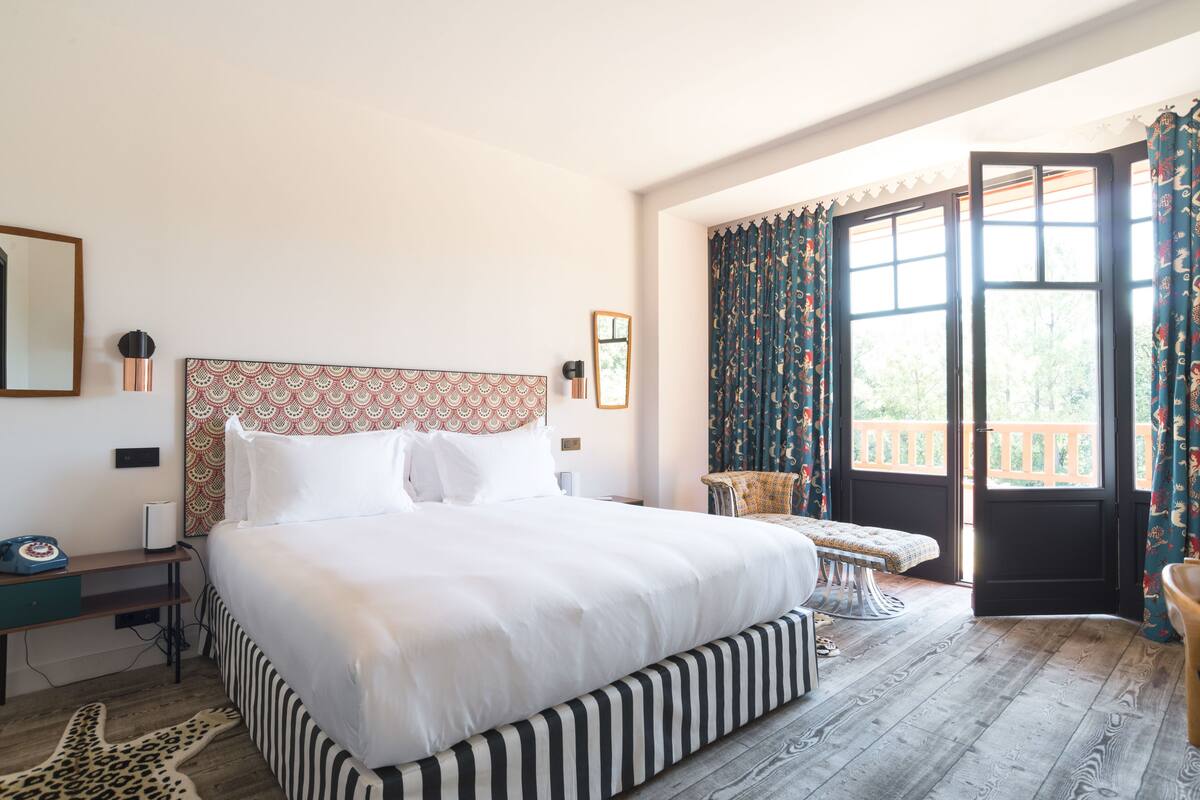 A large bed with a patterned headboard, a bedside table with a telephone, and a bench by the window.