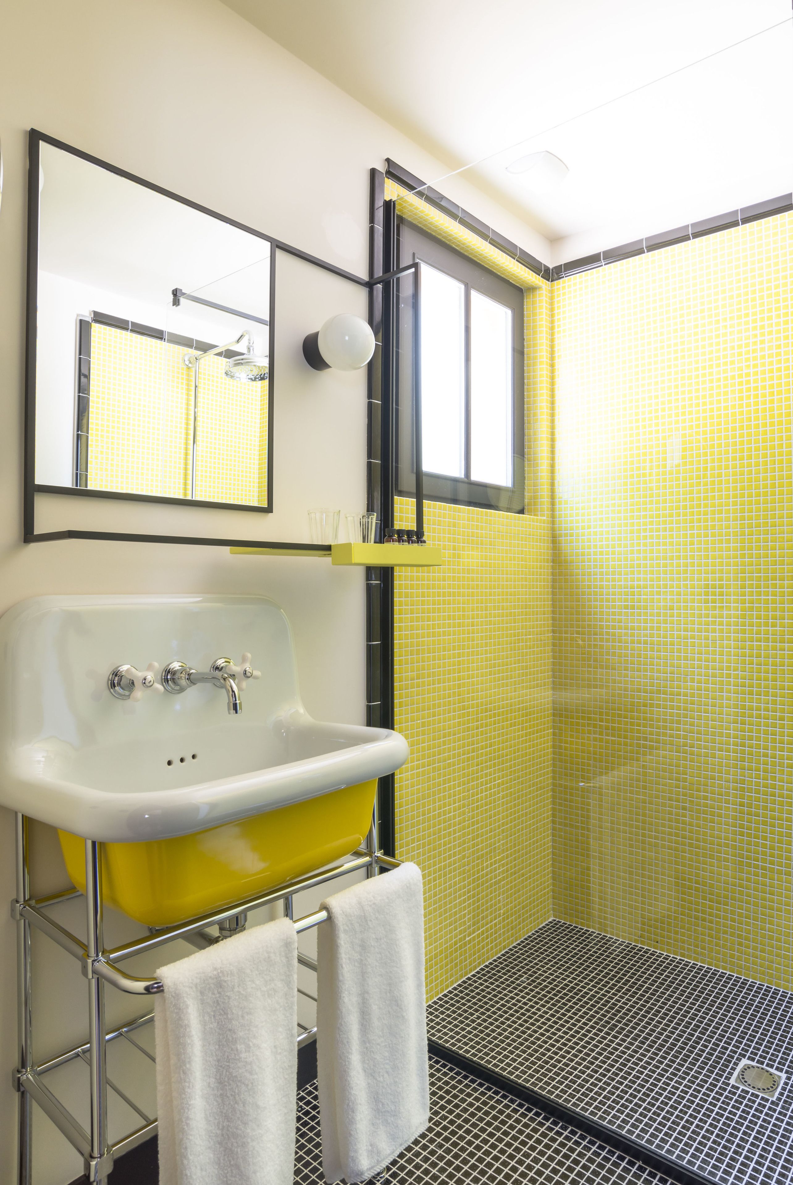 Une salle de bain avec une douche carrelée de carreaux jaunes, un lavabo blanc avec des robinets chromés et un miroir au-dessus du lavabo.