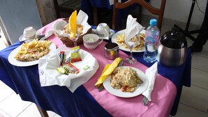 A dining table with various dishes, including a plate of fries, a sandwich, and a dessert. There are also condiments, a bottle of water, and a thermos on the table. - Hôtel La Renardière (Douala)