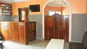 A reception area with a wooden reception desk, a television mounted on the wall, and a large wooden door. - Hôtel La Renardière (Douala)
