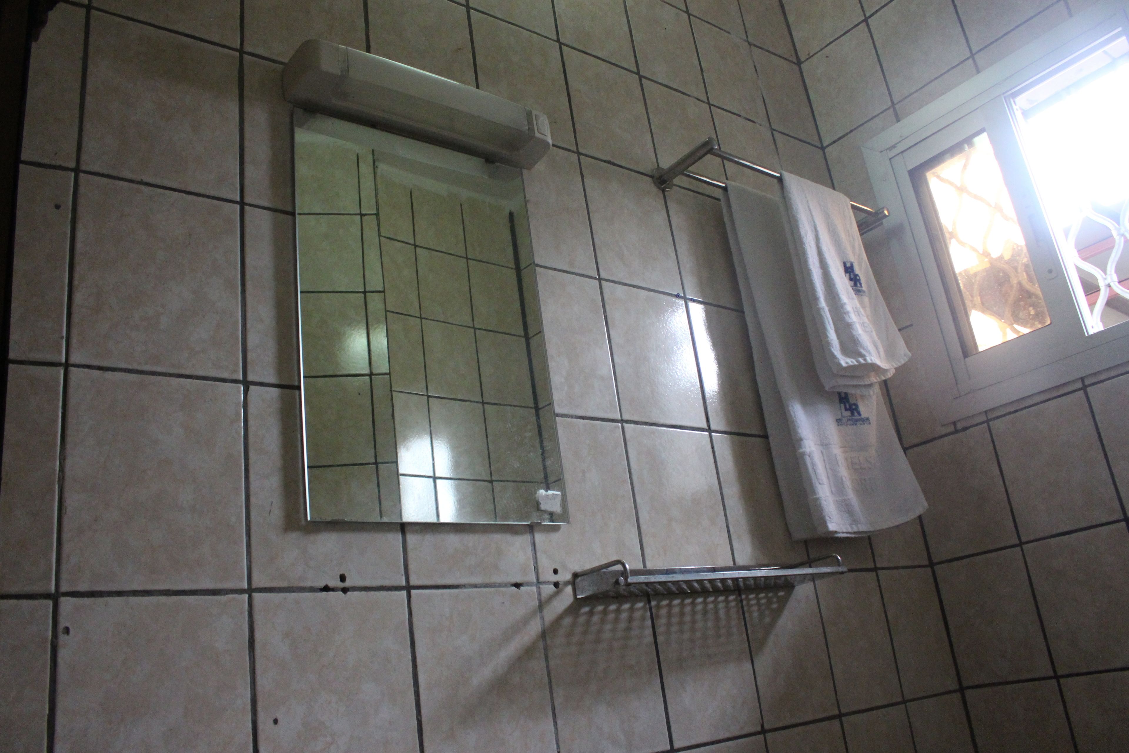 A bathroom with tiled walls, a mirror, a towel rack, and a window.