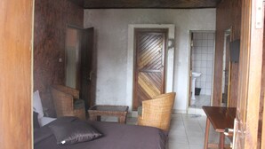A room with a bed, two wicker chairs, a small table, and a wooden door. - Hôtel La Renardière (Douala)