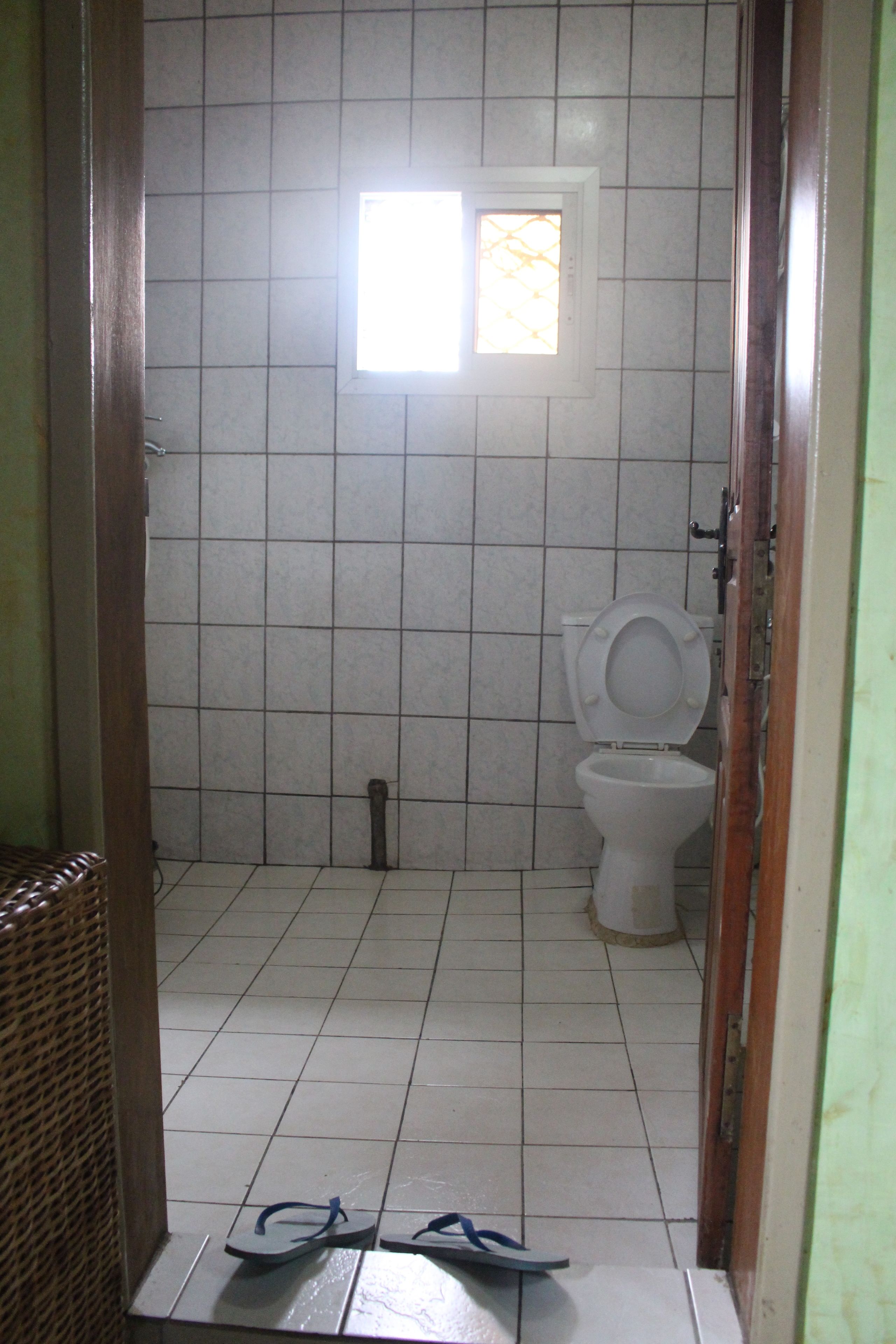 Casa de banho com sanita, janela e um par de chinelos no chão.