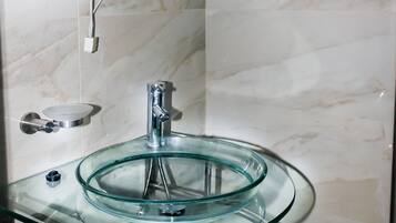 A bathroom with a glass sink, a chrome faucet, and a marble wall.