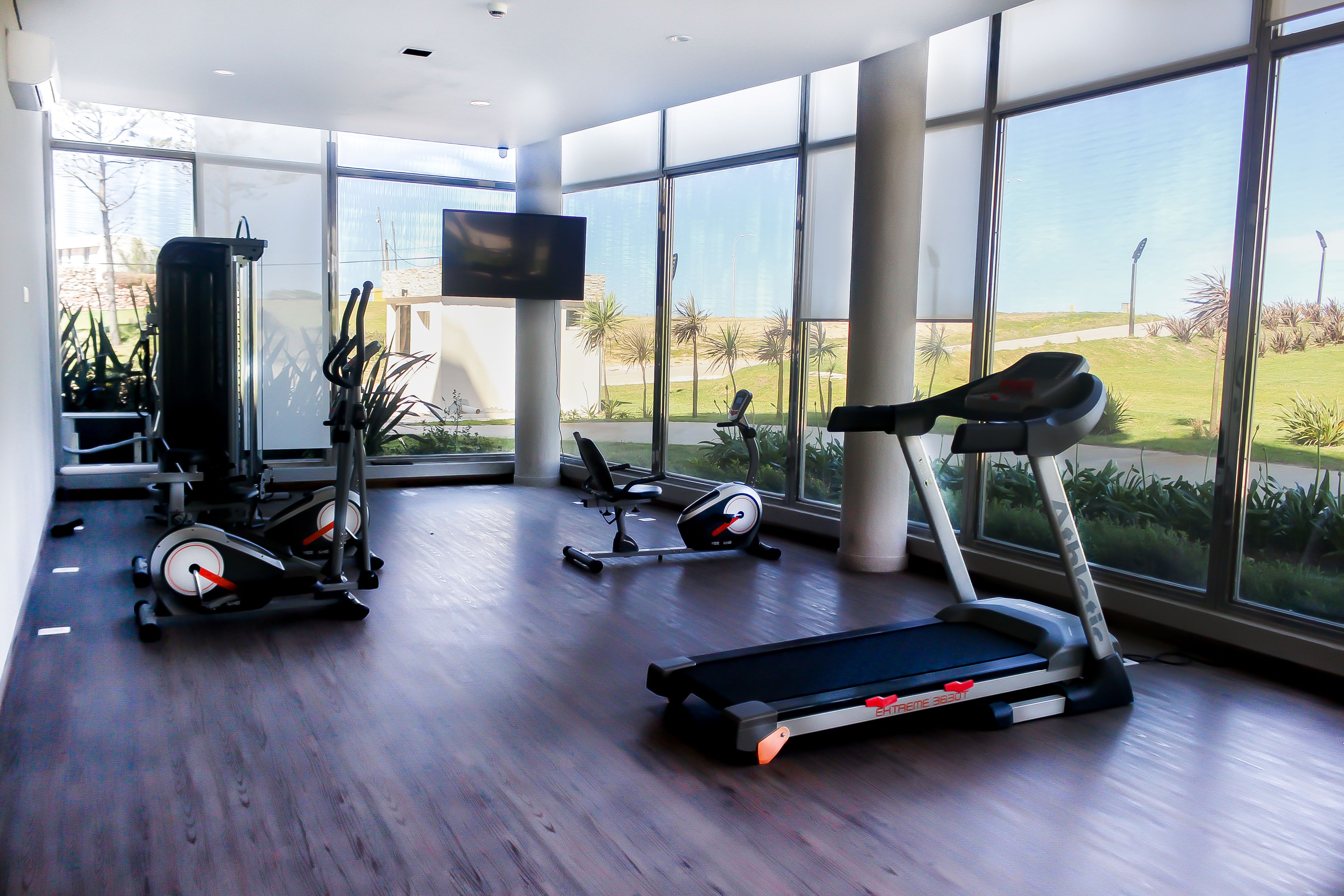 A modern gym with large windows, exercise equipment, and a flat-screen TV.