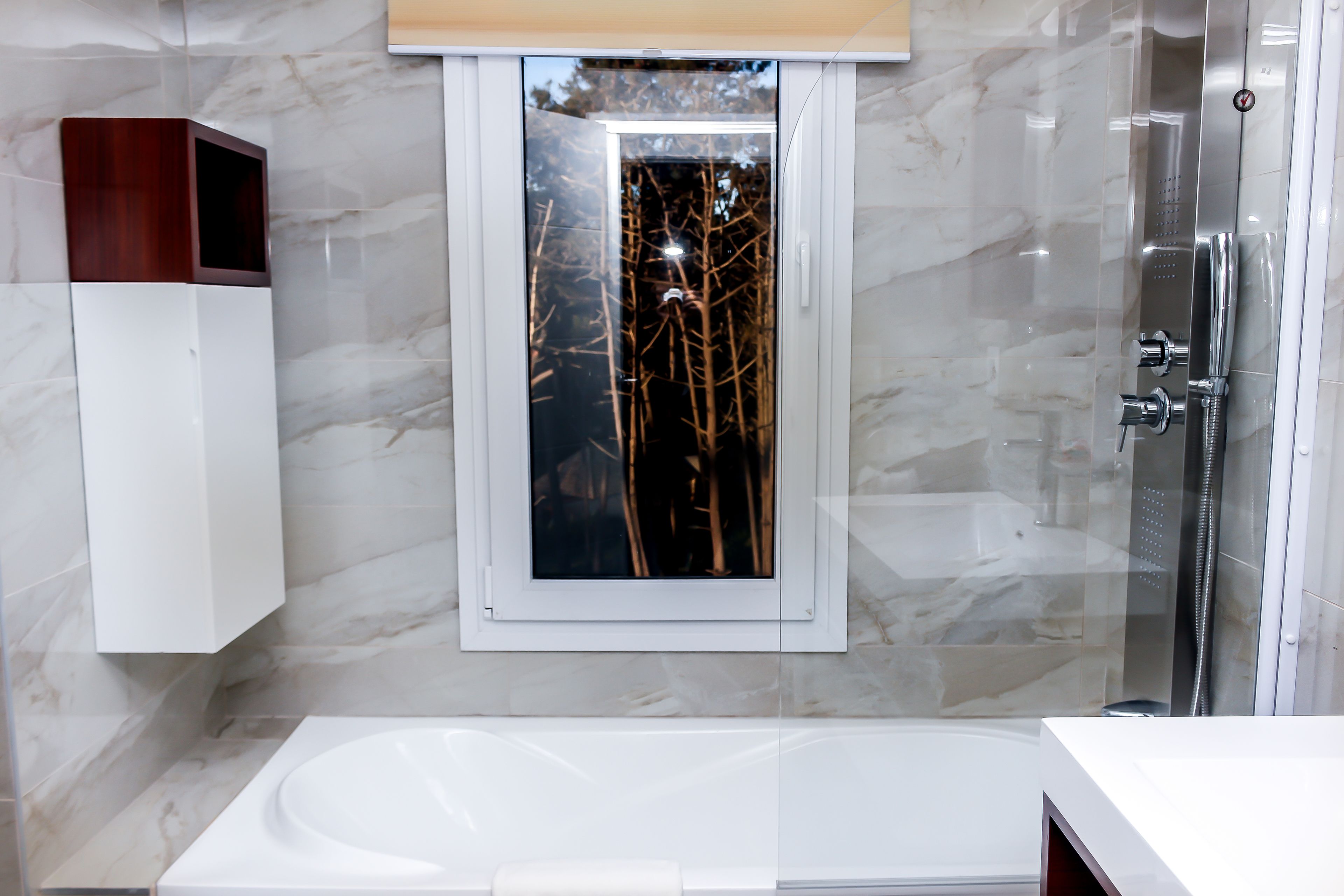 Un baño moderno con una bañera grande, una ducha con mampara de vidrio y un armario de medicinas de madera.