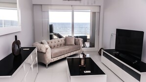 Un salon moderne avec un canapé, une table basse, un téléviseur et une vue sur l’océan.