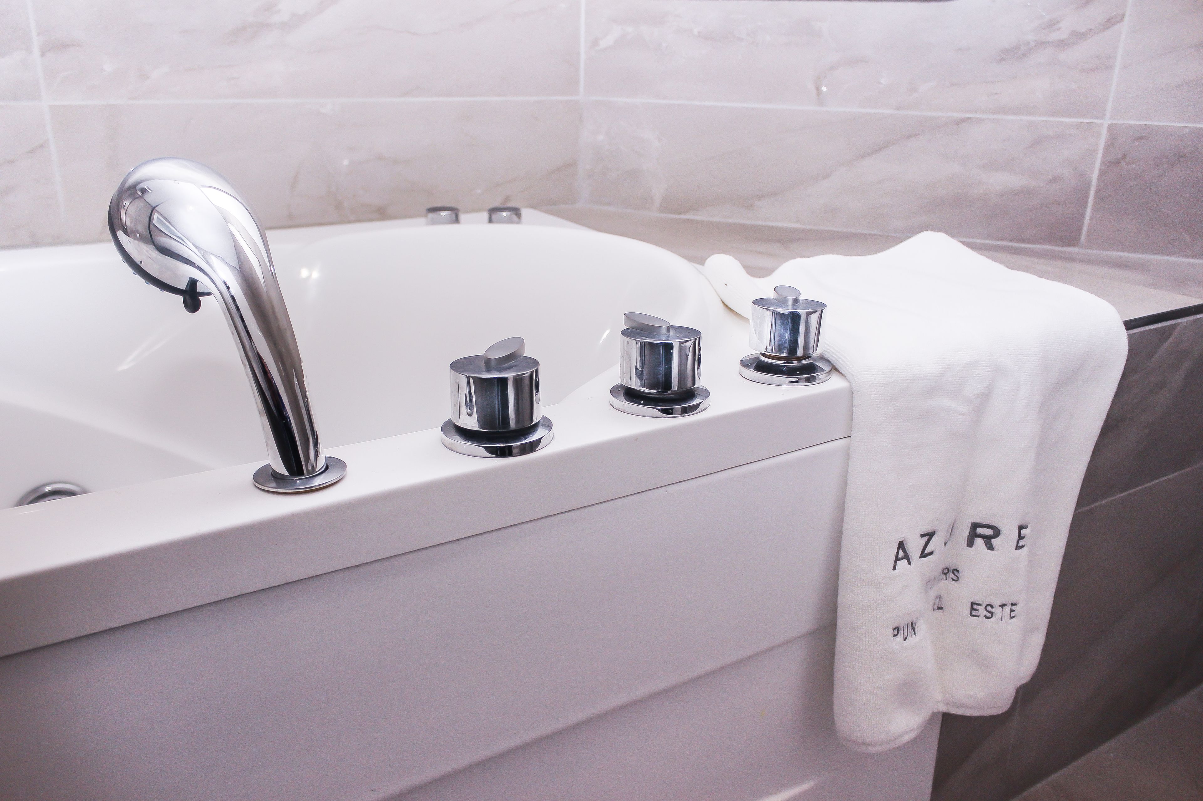 A modern bathroom with a white bathtub, chrome faucets, and a towel with text hanging on the wall.