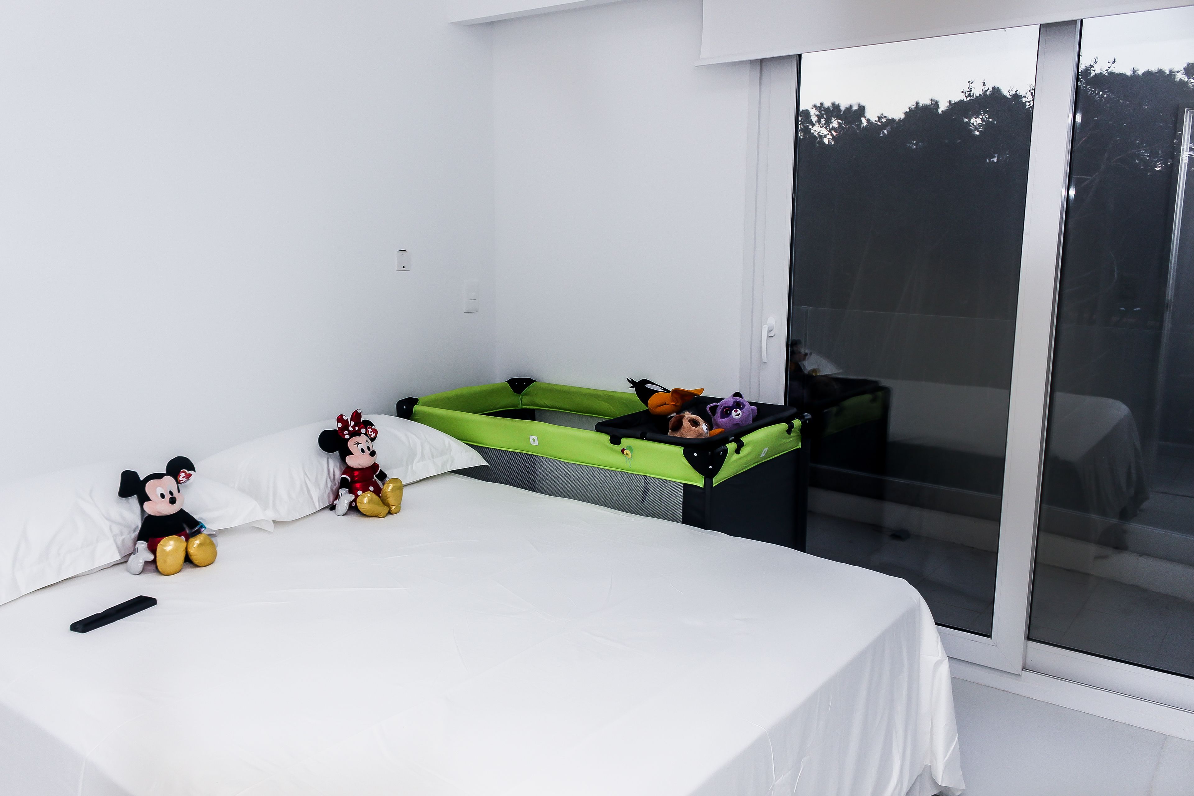 A modern hotel room with a large bed, a green sofa bed, and Mickey and Minnie Mouse plush toys.