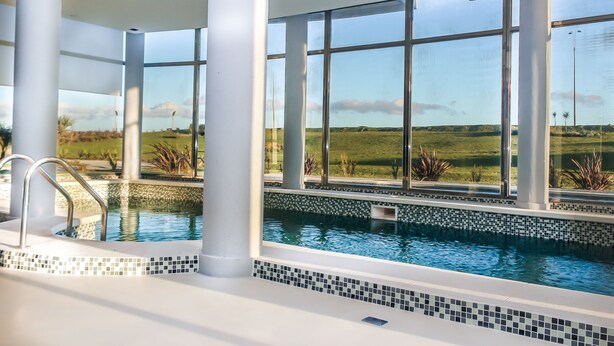 Une piscine intérieure moderne, dotée de grandes fenêtres qui offrent une vue sur un paysage verdoyant.