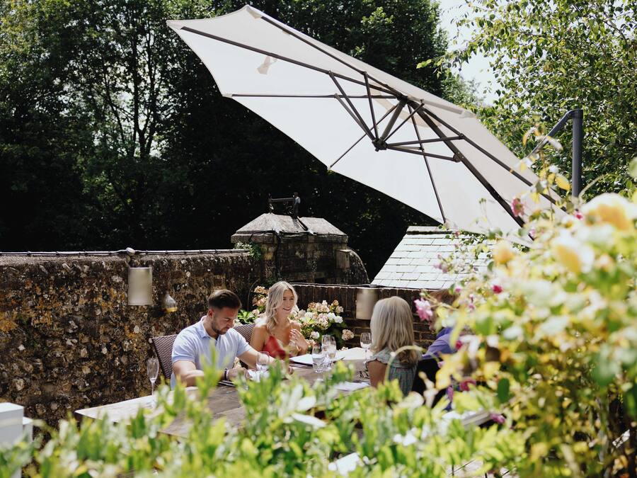 An outdoor dining area with stone walls, a large umbrella, and a rustic thatched roof structure.