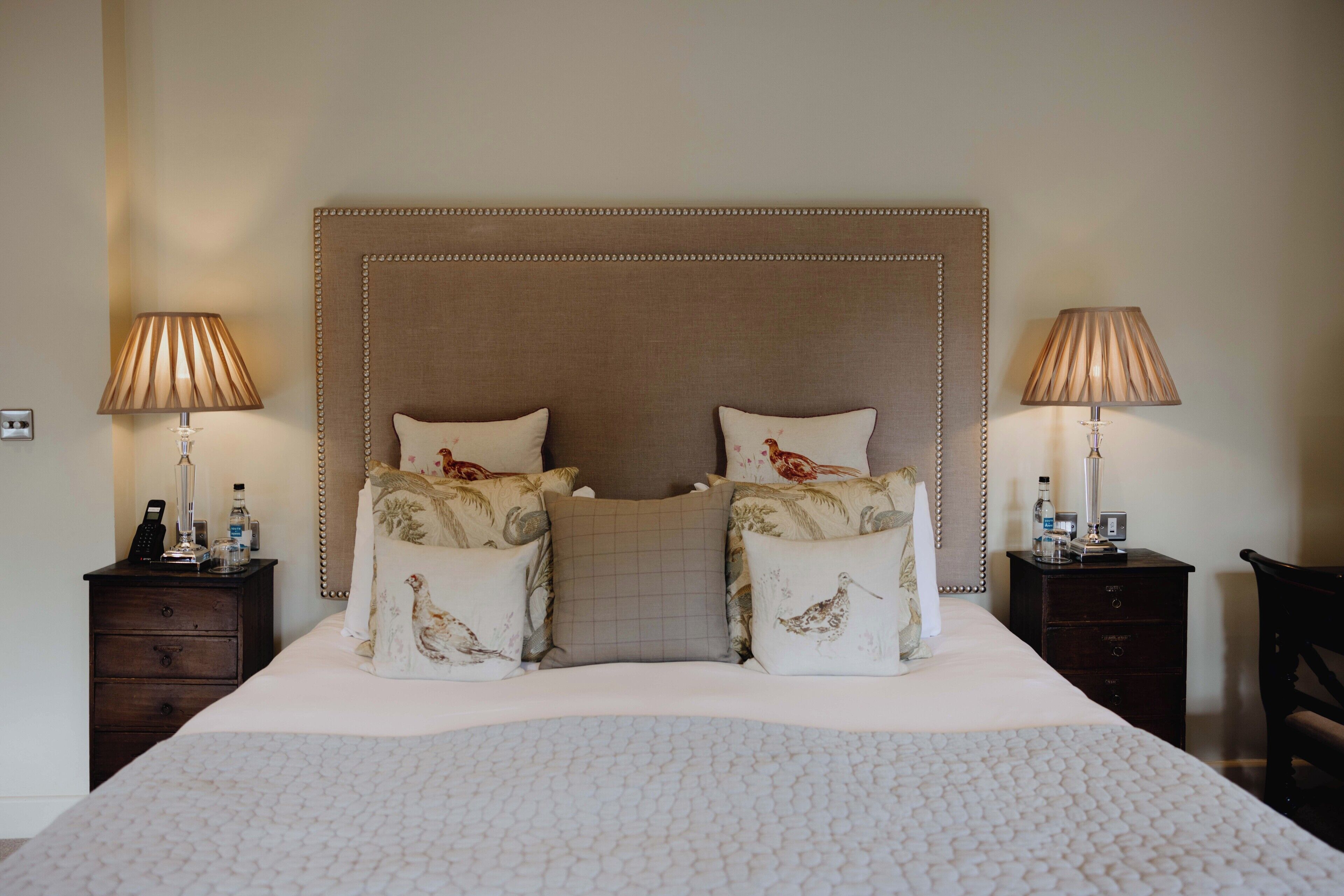 Una cama bien hecha con un cabecero capitonado, dos mesitas de noche con lámparas y almohadones decorativos.