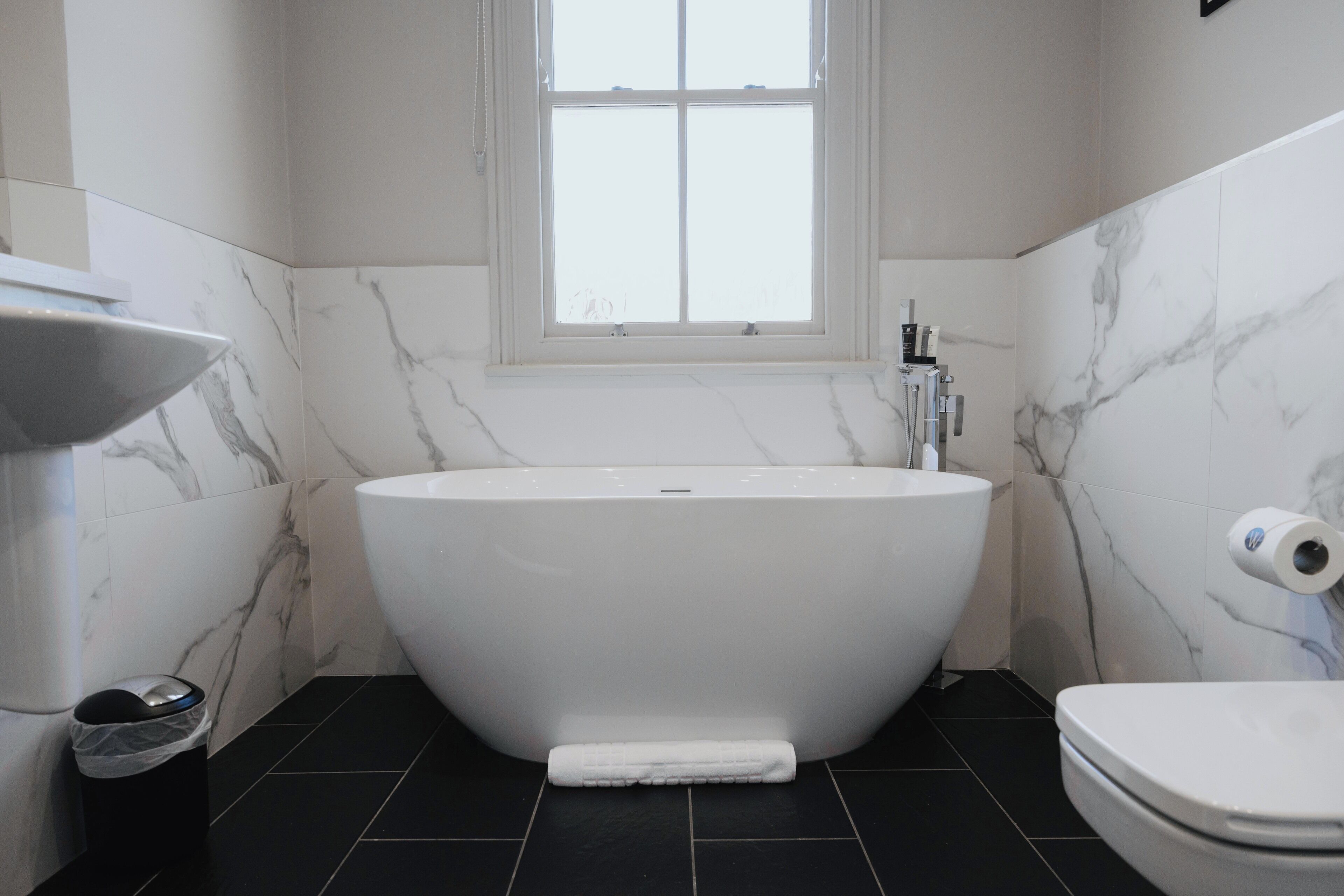 Ein Badezimmer mit einer freistehenden Badewanne, einer Toilette und einem Fenster über der Badewanne.