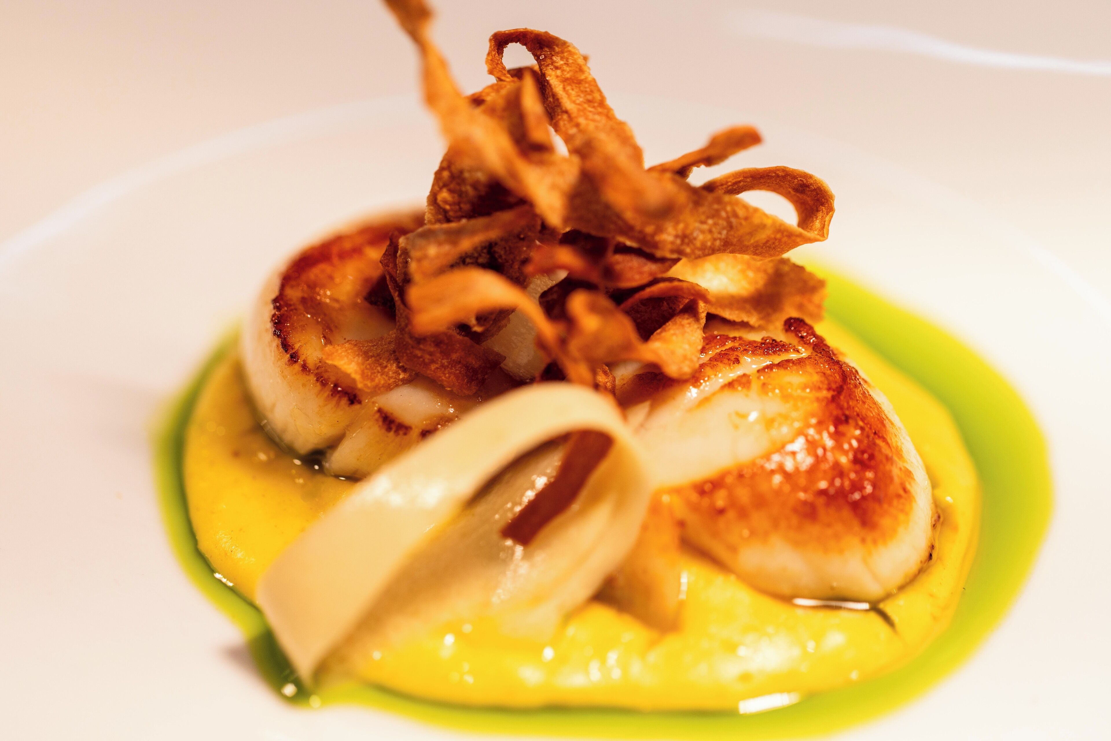 A plate of food with seared scallops, crispy bacon, and a green sauce.