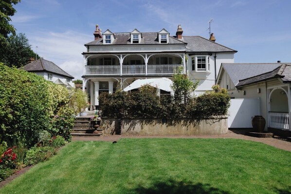 A two-story house with a balcony, a garden, and a white umbrella.