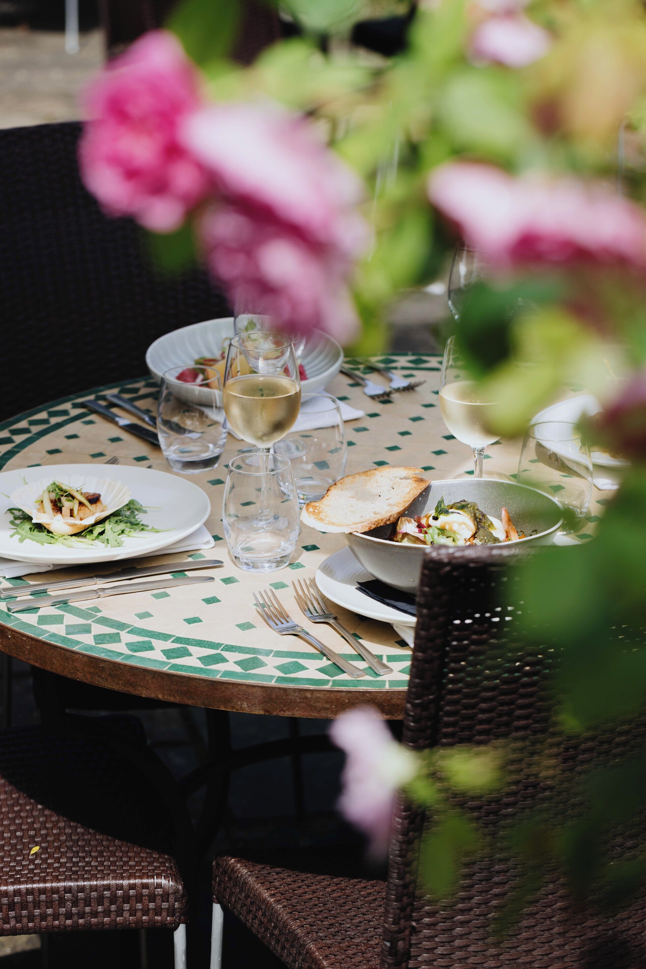 A round dining table with plates of food, glasses of white wine, and cutlery.