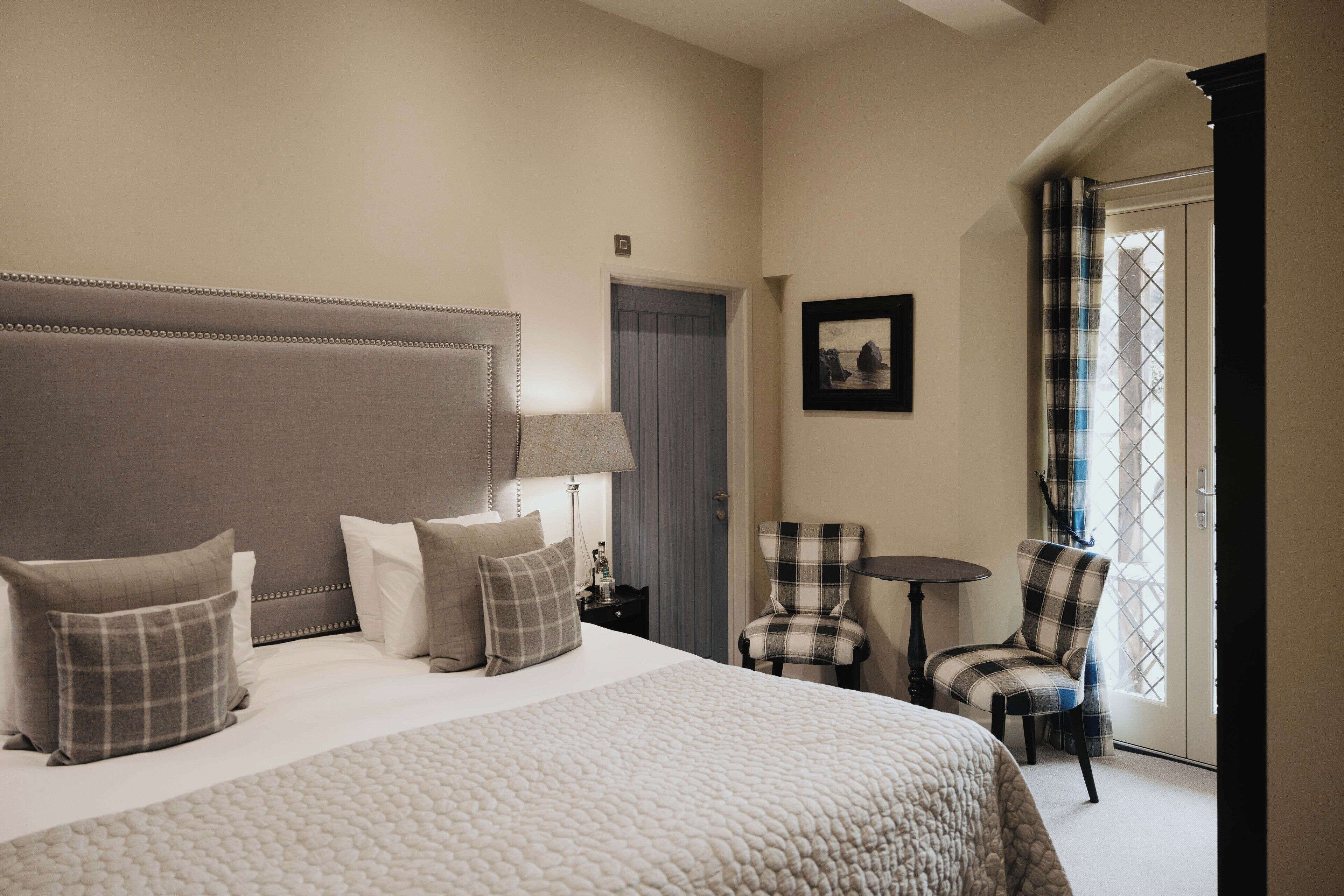 Una habitación de hotel con una cama grande, una silla, una mesita y una puerta que da a un balcón.