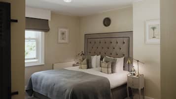 A bedroom with a large bed, a bedside table with a lamp, a radiator, and framed pictures on the wall.