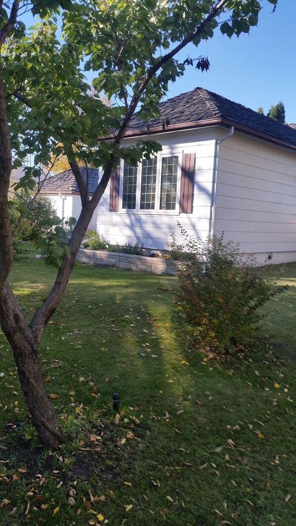 Una casa con facciata bianca, tetto scuro e un piccolo giardino davanti con erba e un albero.