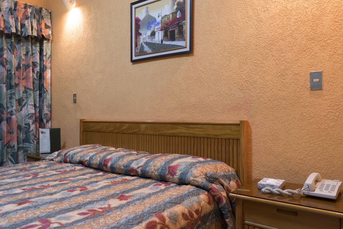 Een hotelkamer met een bed, een nachtkastje met telefoon en een lijst aan de muur.