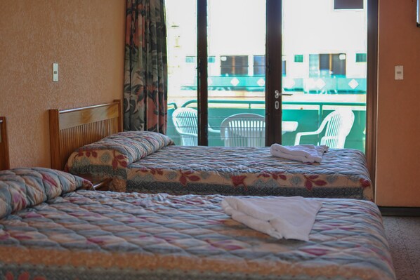 Habitación de hotel con dos camas, vista al exterior y un balcón con sillas.