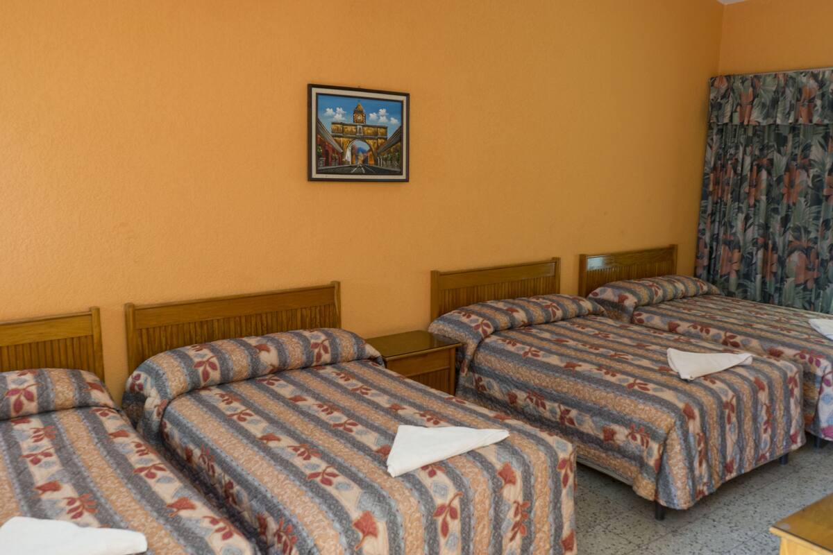 Een hotelkamer met drie bedden, een houten hoofdeinde, een ingelijste foto aan de muur en een bloemenprint gordijn.