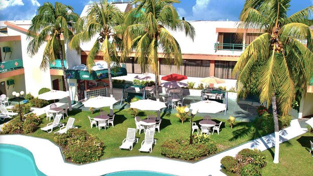 Zona de piscina en un resort con sillas de descanso, sombrillas y palmeras.