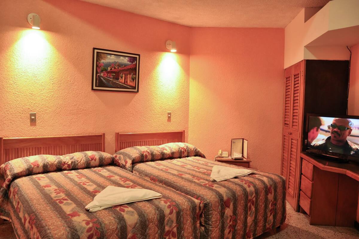 Een hotelkamer met twee bedden, een televisie en een schilderij aan de muur.