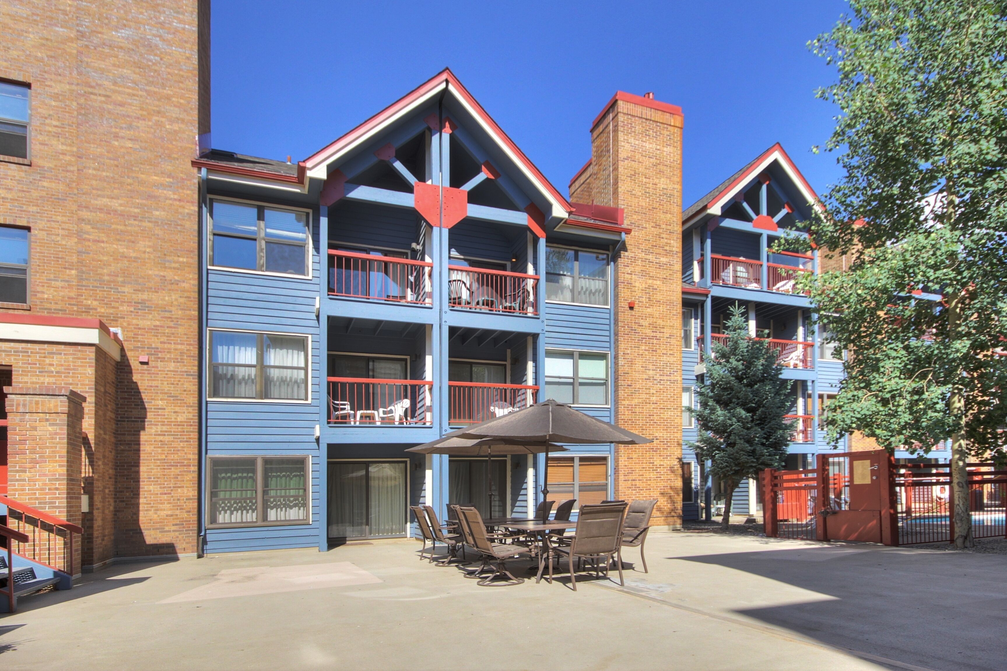 A multi-story building with balconies, a patio area with outdoor furniture, and a brick facade.