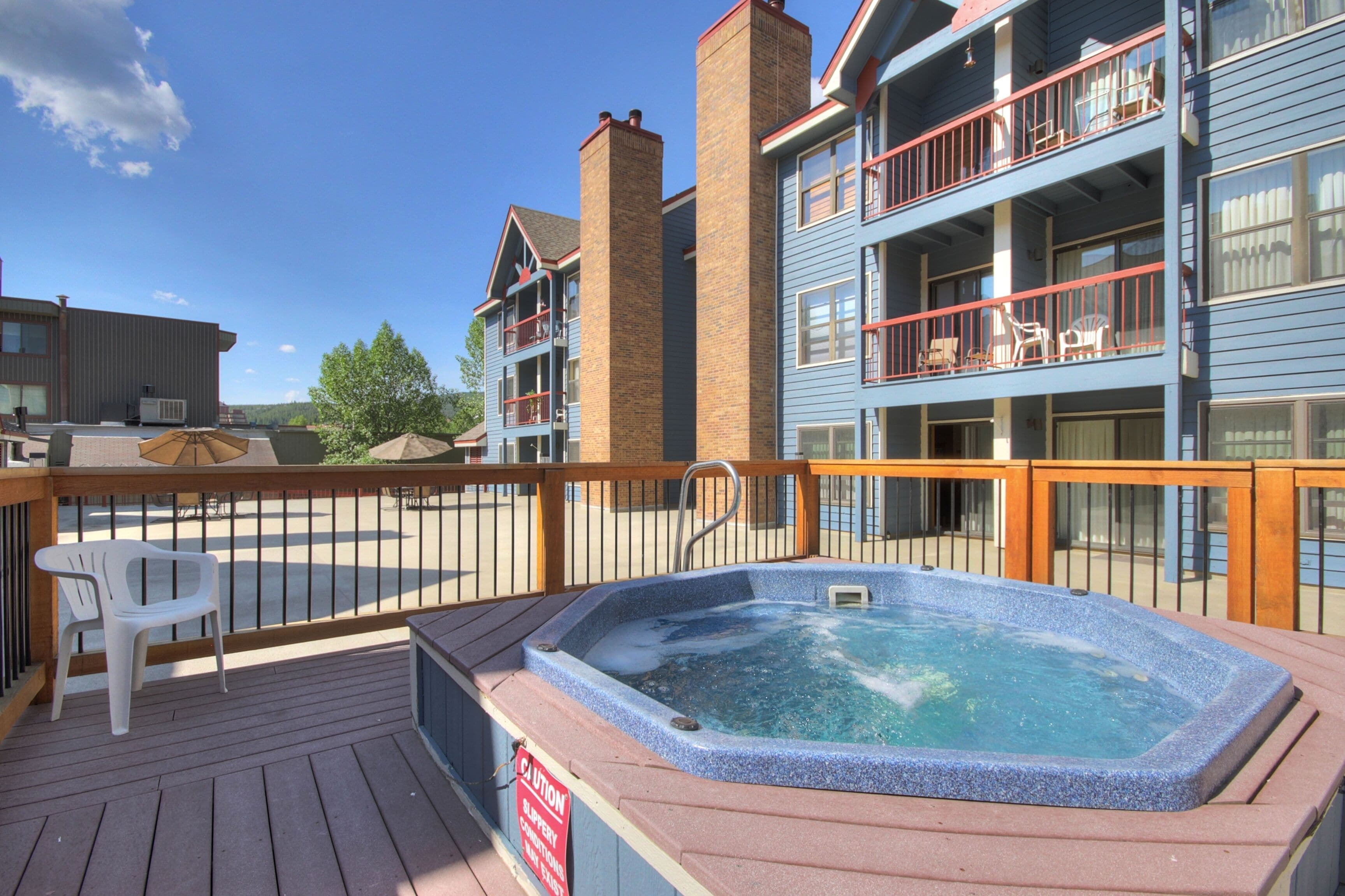A hot tub on a wooden deck with a caution sign, surrounded by a wooden railing.