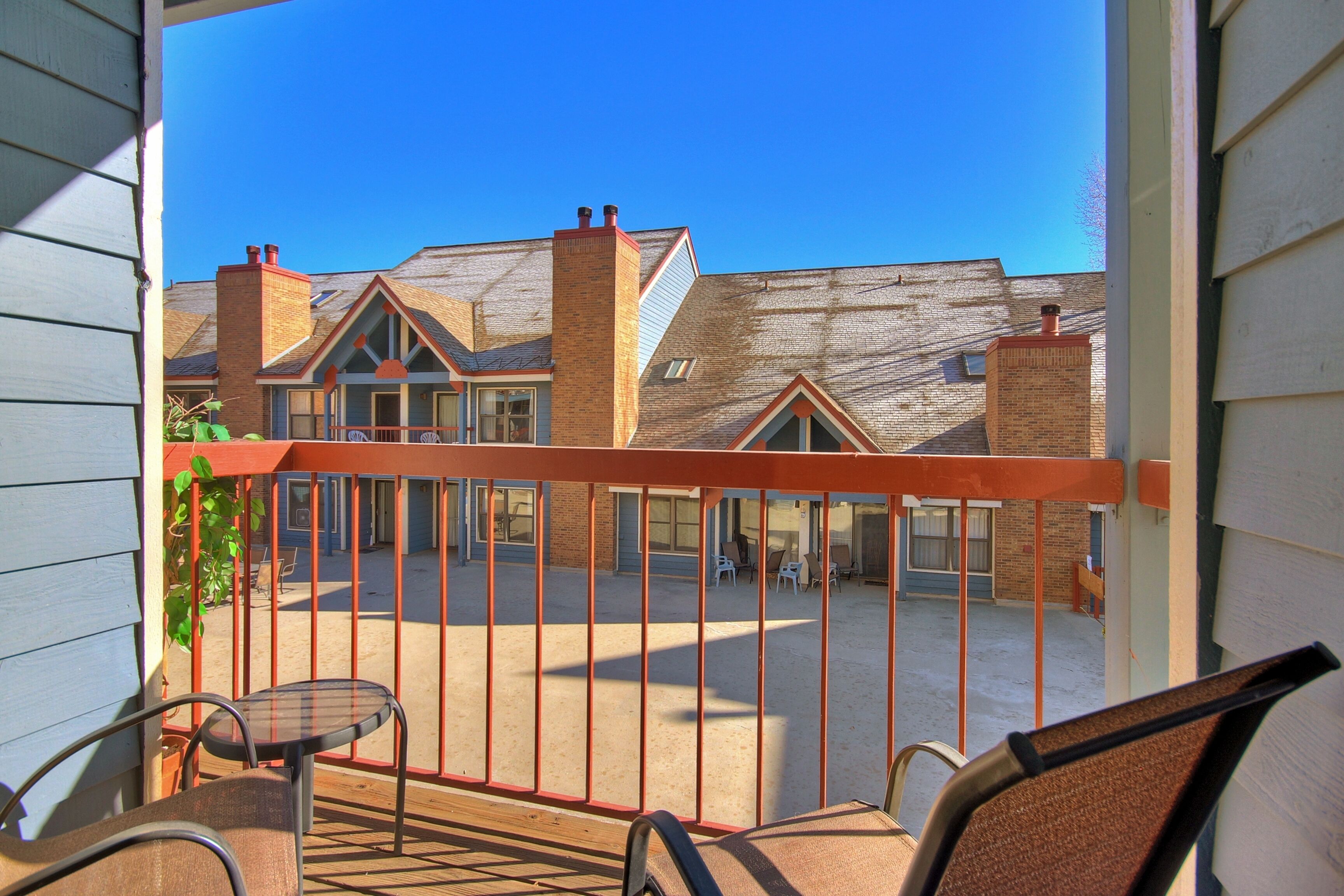 A balcony with a view of a building with brick chimneys and a clear blue sky.