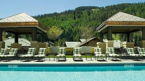 Zona de piscina con sillas de descanso y gazebos, rodeada por una ladera boscosa.