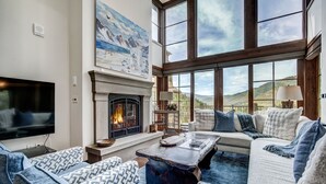 Una sala de estar con chimenea, ventanas amplias y un televisor.
