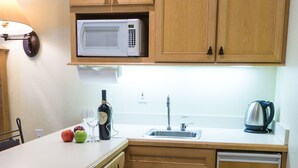 A compact kitchen with wooden cabinets, a microwave, a sink, and a kettle.
