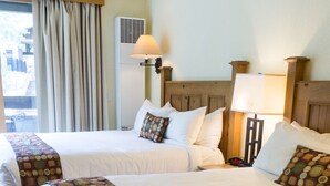 A hotel room with two beds, each with a patterned bedspread, a wooden headboard, and a bedside table with a lamp.