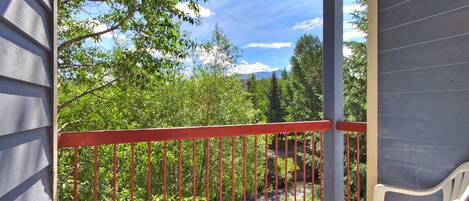 A balcony with a red railing, overlooking a lush green landscape with trees and a stream.