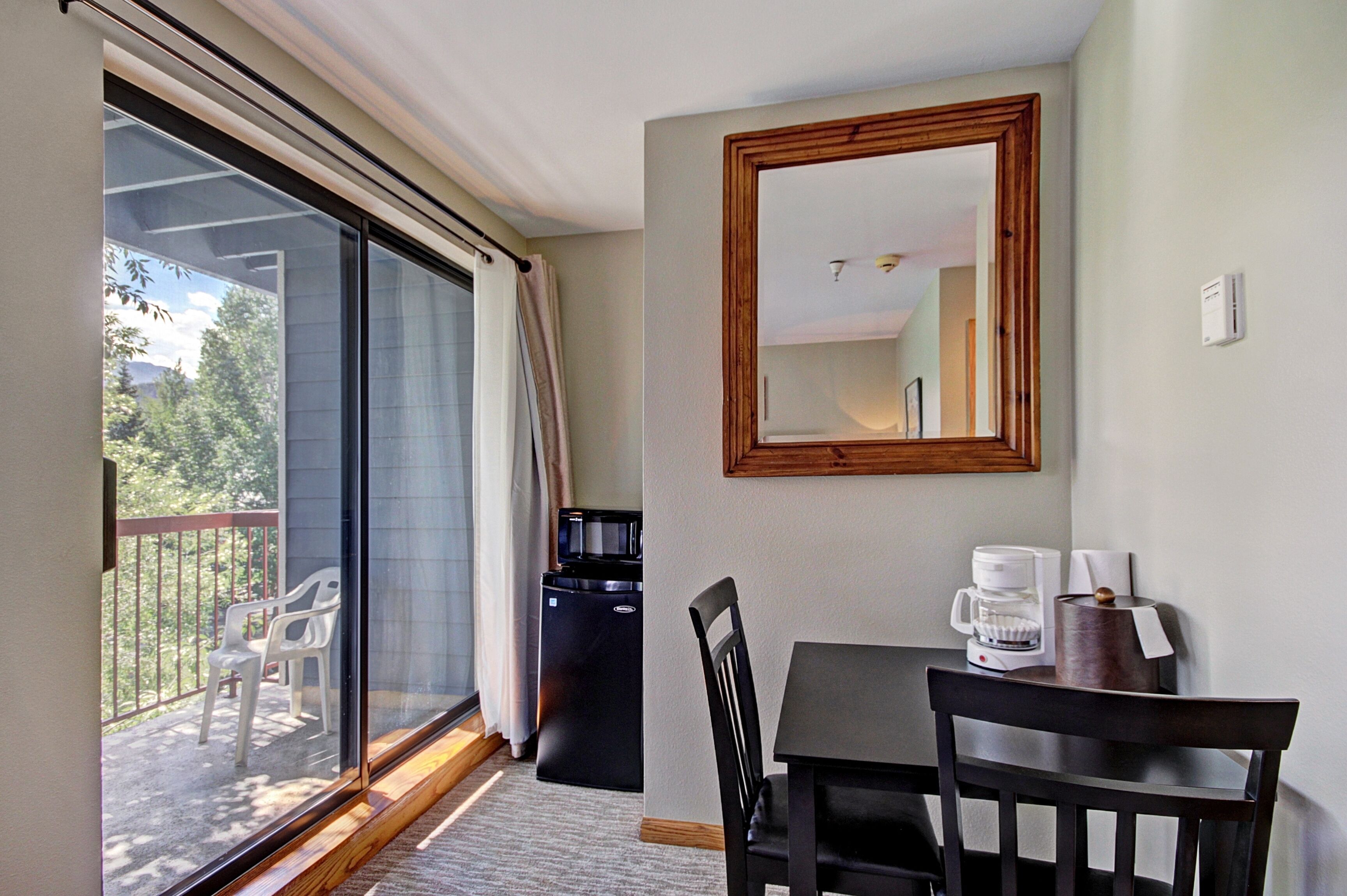 A room with a dining table, chairs, a coffee maker, a microwave, and a sliding glass door leading to a balcony with chairs.