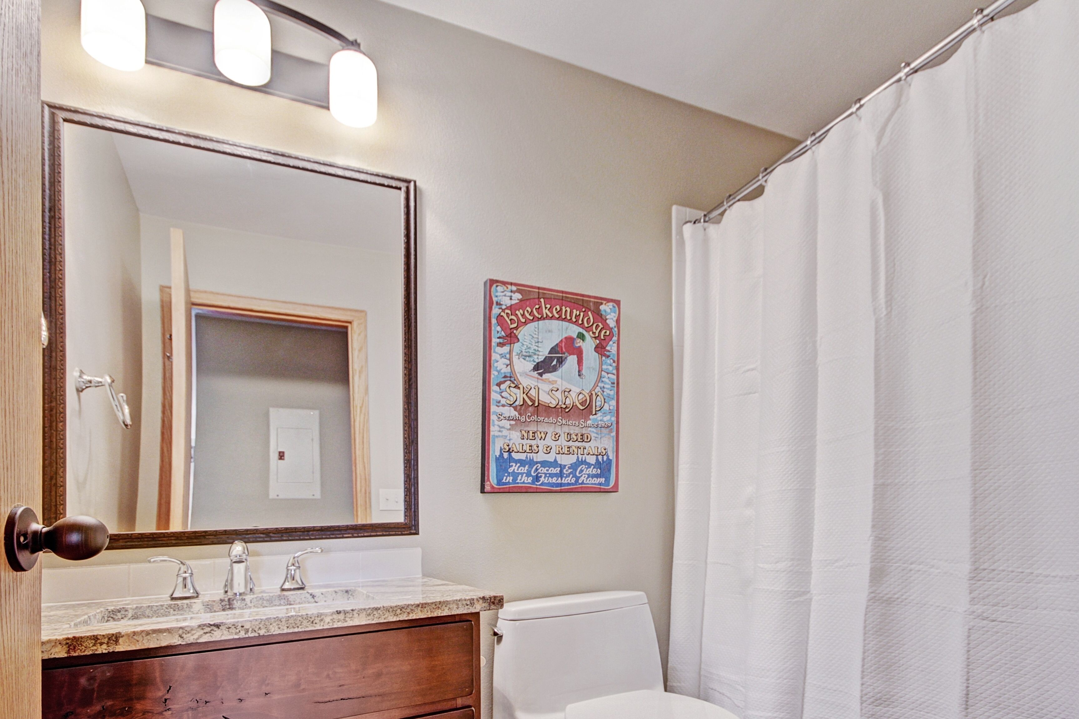A bathroom with a large mirror, a sink, a toilet, and a shower curtain.
