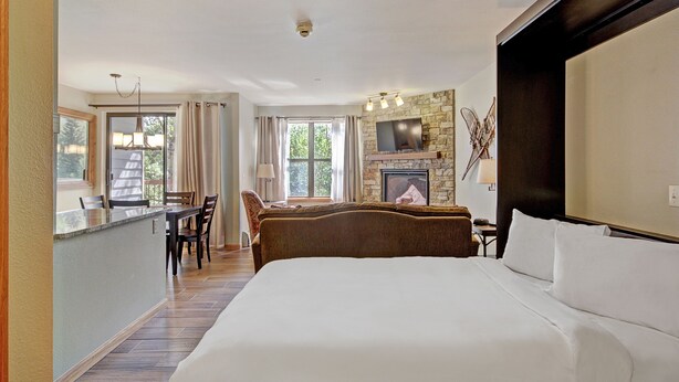 Ein Hotelzimmer mit einem großen Bett, einer Essecke mit Tisch und Stühlen, einem Kamin und einem an der Wand befestigten Fernseher.
