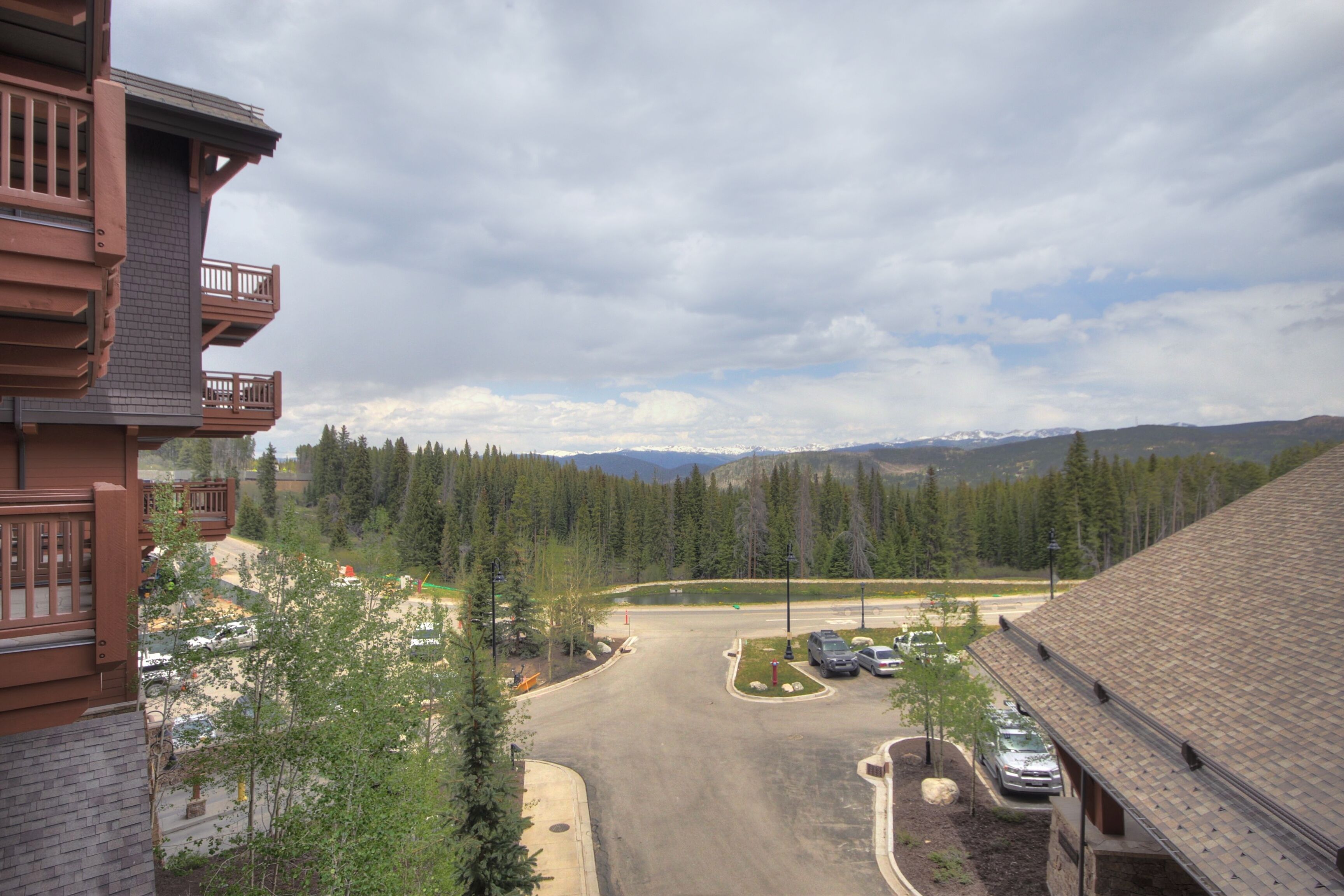 A mountain lodge with a parking area, a view of the surrounding forest, and a distant mountain range.