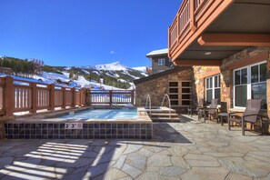 A pool area with a stone deck, lounge chairs, and a view of a snow-covered mountain.