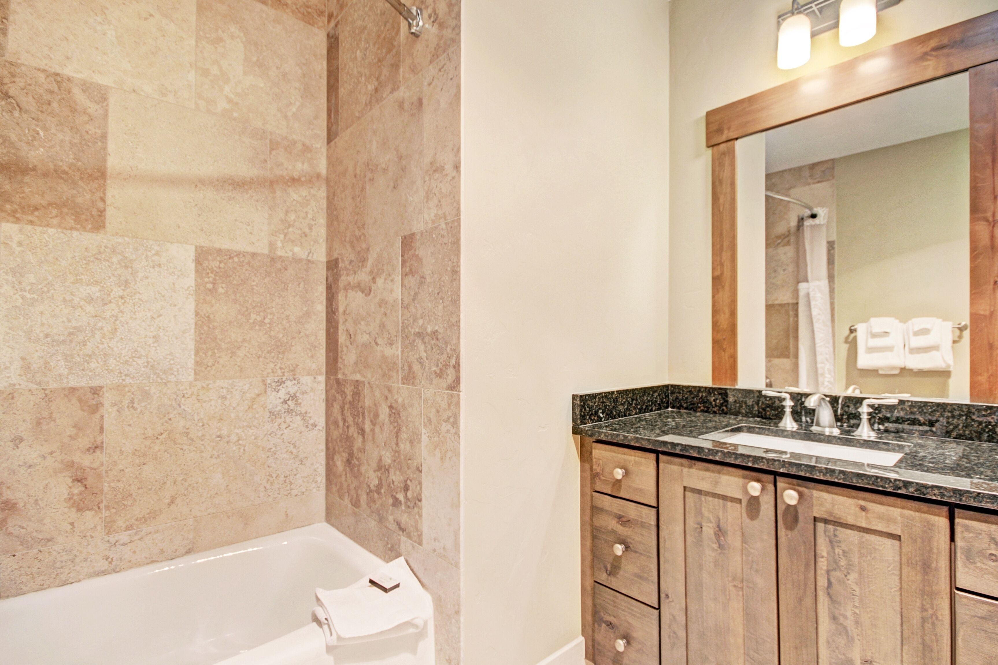 Un baño con bañera, tocador de madera con lavamanos y un espejo grande.