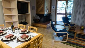 A dining area with a wooden table set for a meal, a television on a shelf, a fireplace, and a view of the outdoors. - Gold Bend 5022 (Truckee)