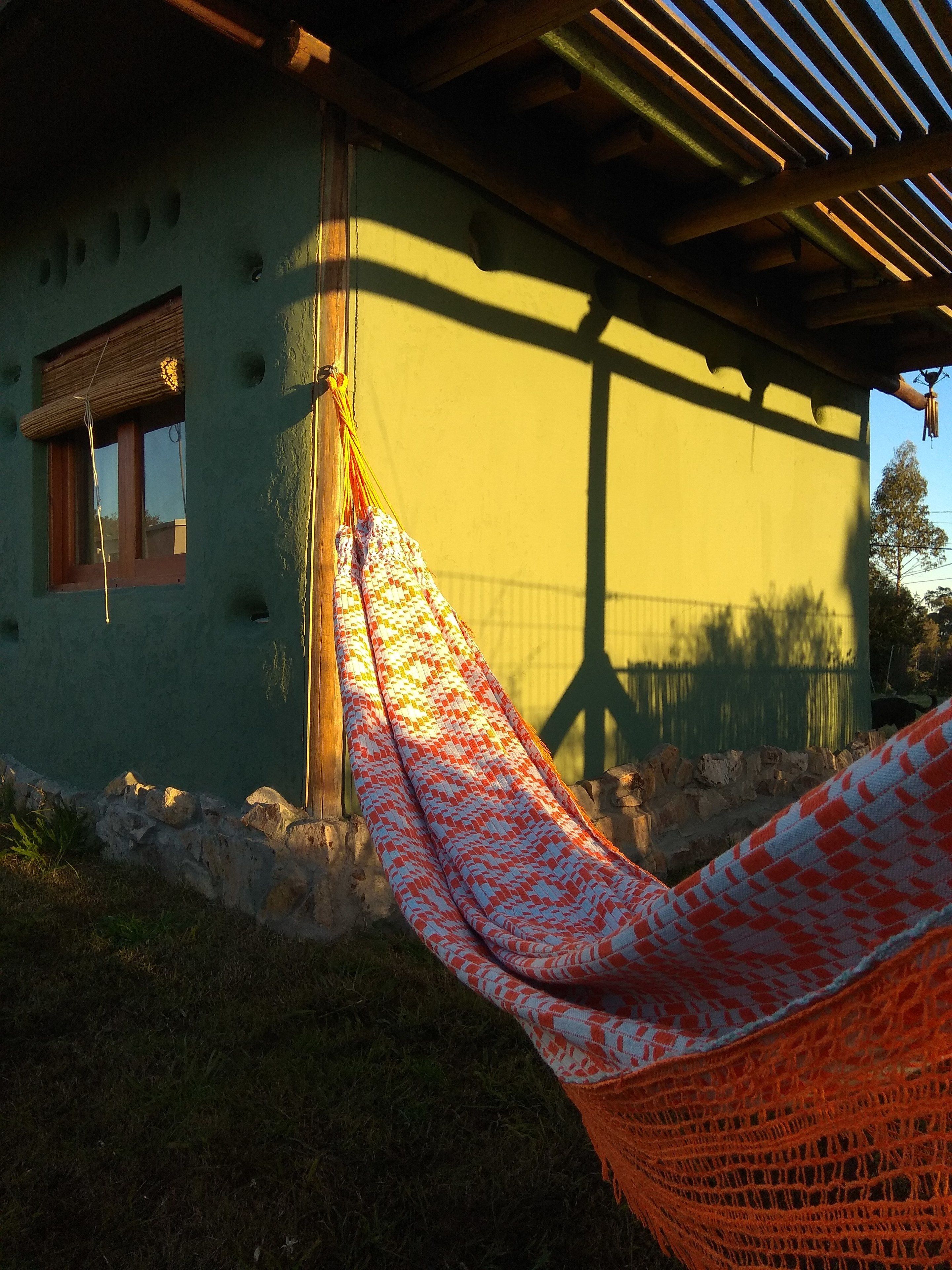 A hammock tied to a wooden post under a wooden pergola, with a green building in the background.
