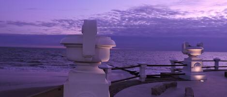 A coastal walkway with white stone balustrades and a bench.