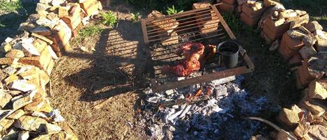 A circular fire pit with a grill and a pot, surrounded by bricks and rocks.