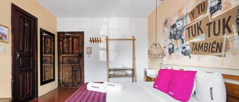 A hotel room with a bed, pillows, a wooden wardrobe, a ceiling fan, and a wall with a mural.