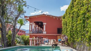Un espace piscine avec un bâtiment rouge, des sièges en plein air et de la verdure.