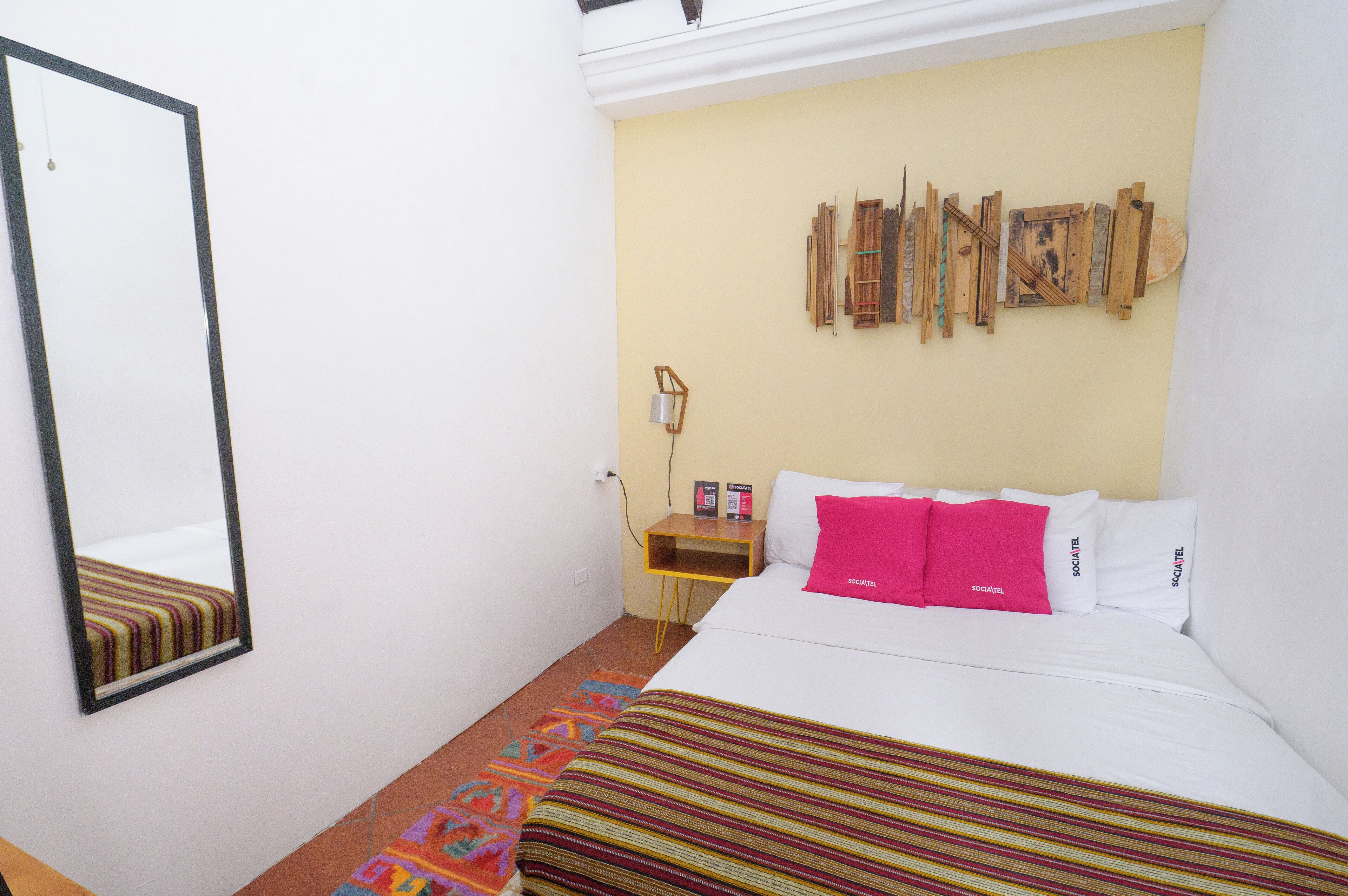 Une chambre d’hôtel avec un lit, une table de chevet, un miroir et un mur orné d’œuvres d’art en bois.